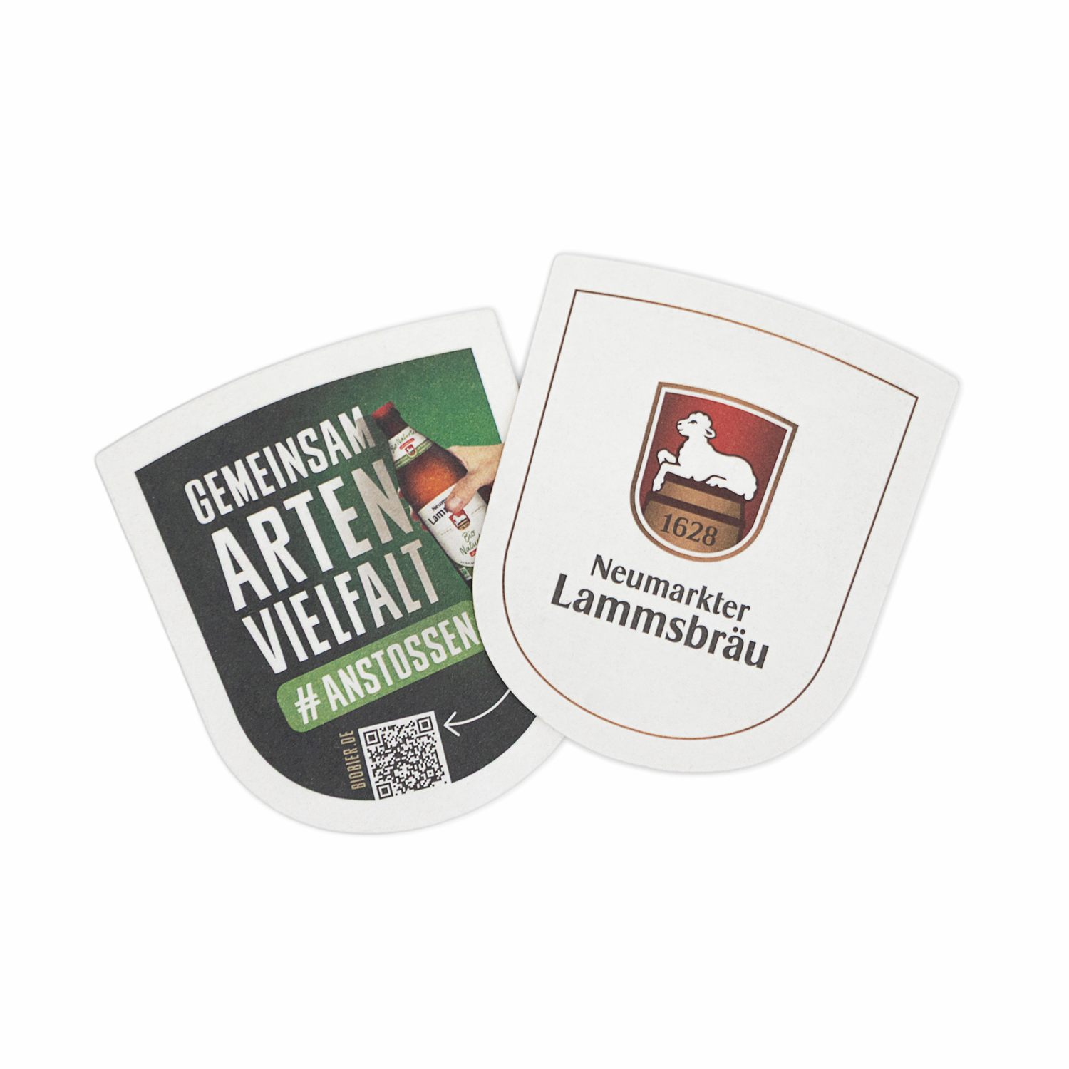 Zwei wappenförmige Bierdeckel liegen leicht überlappend in der Draufsicht auf weißem Hintergrund. Der rechte Deckel zeigt das Neumarkter Lammsbräu-Wappen auf weißem Grund, während der linke die dunkle Rückseite mit dem Text „GEMEINSAM ARTEN VIELFALT #ANSTOSSEN“, einer abgebildeten Bierflasche und einem QR-Code präsentiert.