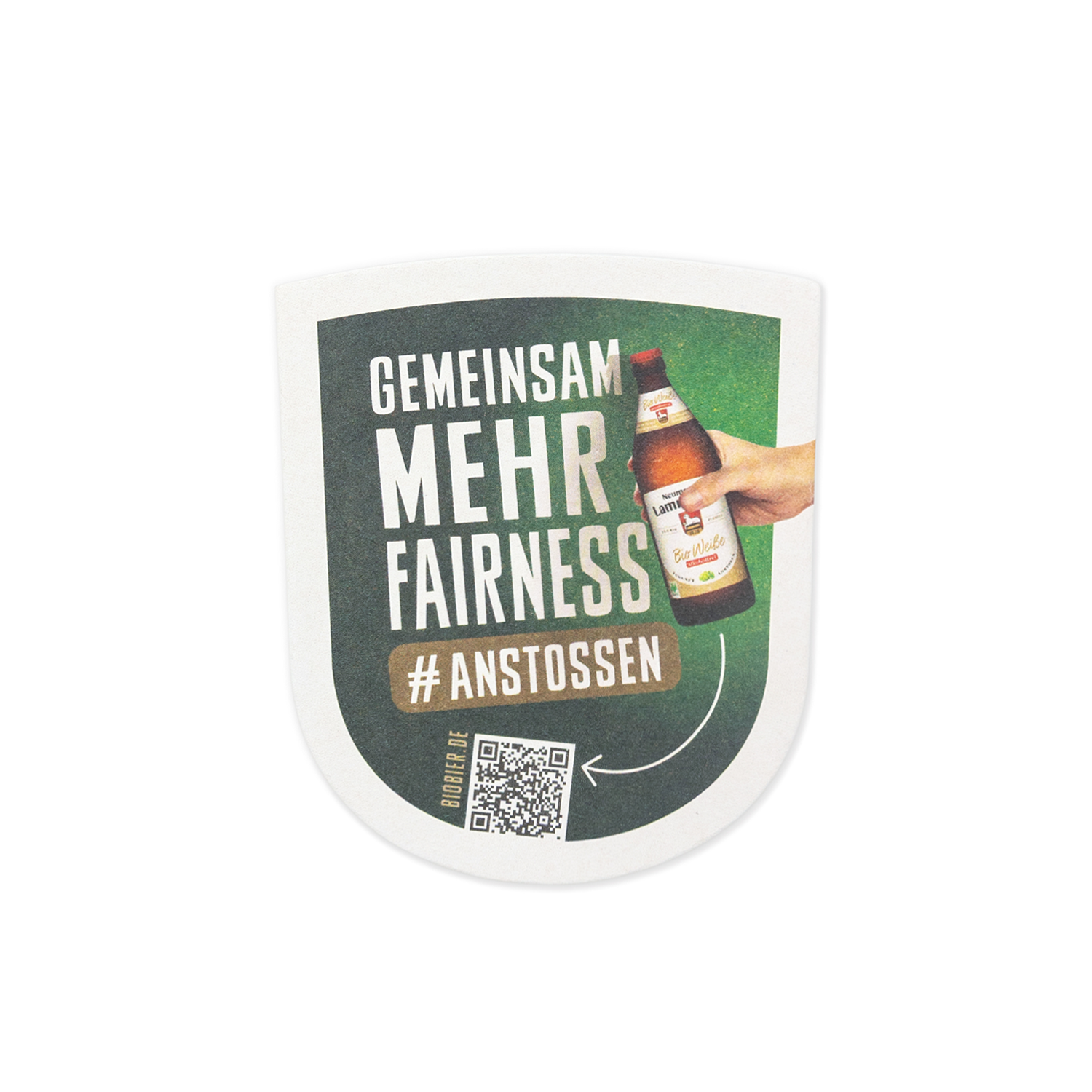 Wappenförmiger Bierdeckel auf weißem Hintergrund. Die obere Hälfte zeigt auf dunkelgrünem Hintergrund den weißen Text „GEMEINSAM MEHR FAIRNESS" und das Hashtag „#ANSTOSSEN". Daneben eine fotografierte Hand, die eine dunkelbraune Neumarkter Lammsbräu-Bierflasche mit hellem Etikett hält. Unten links befindet sich ein schwarzer QR-Code mit der Aufschrift „BIOBIER.DE".