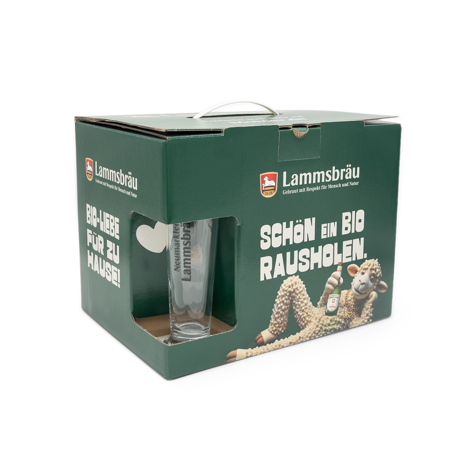 Grüne Lammsbräu-Geschenkbox mit Sichtfenster und Tragegriff in leicht perspektivischer Vorderansicht auf weißem Hintergrund. Das transparente Fenster zeigt ein klares Bierglas mit "Neumarkter Lammsbräu"-Aufschrift. Die Vorderseite trägt das Lammsbräu-Logo, weißen Text "SCHÖN EIN BIO RAUSHOLEN", ein weißes Herz-Symbol und die Lamm-Illustration mit Bierflasche.