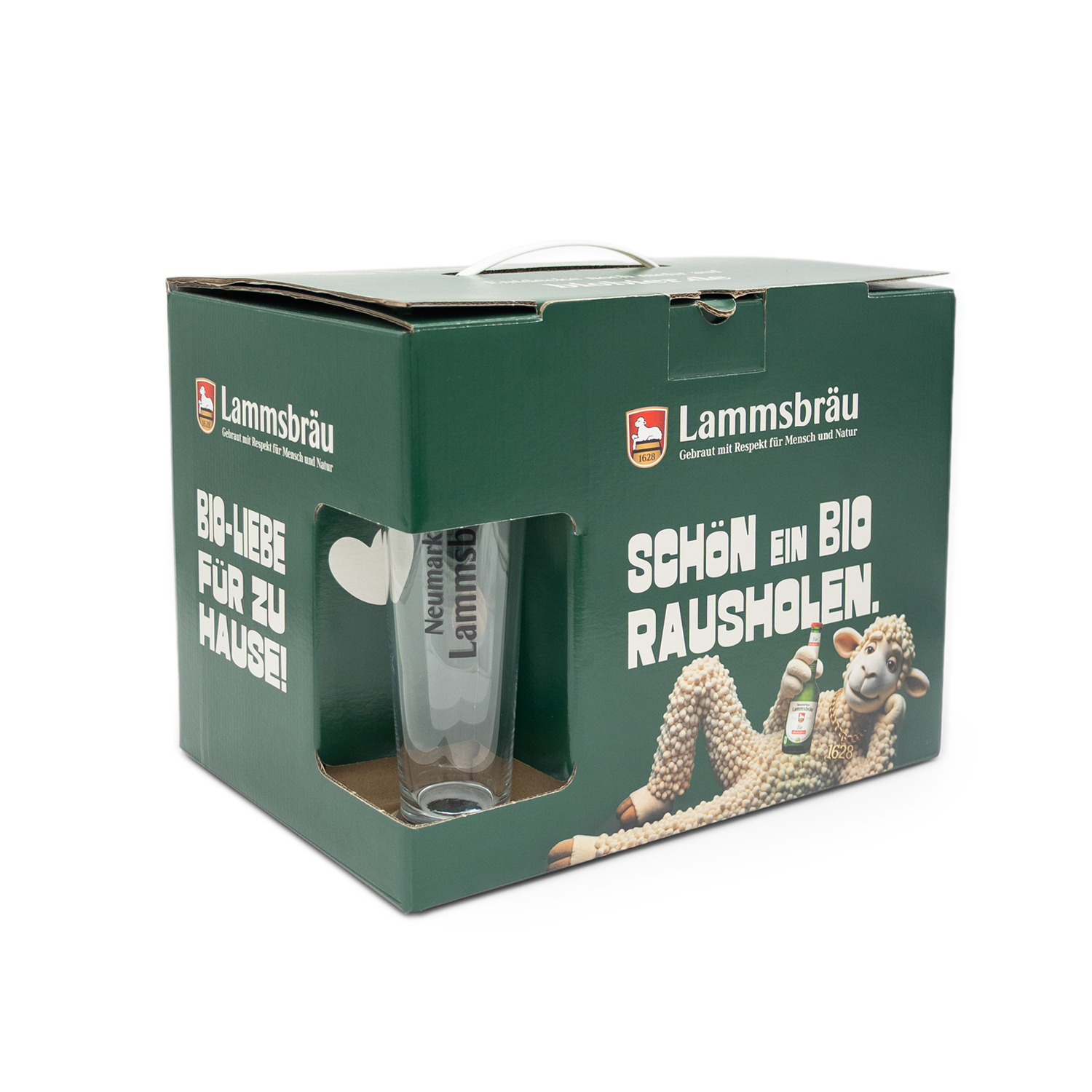 Grüne Lammsbräu-Geschenkbox mit Sichtfenster und Tragegriff in leicht perspektivischer Vorderansicht auf weißem Hintergrund. Das transparente Fenster zeigt ein klares Bierglas mit "Neumarkter Lammsbräu"-Aufschrift. Die Vorderseite trägt das Lammsbräu-Logo, weißen Text "SCHÖN EIN BIO RAUSHOLEN", ein weißes Herz-Symbol und die 3D-Lamm-Illustration mit Bierflasche.