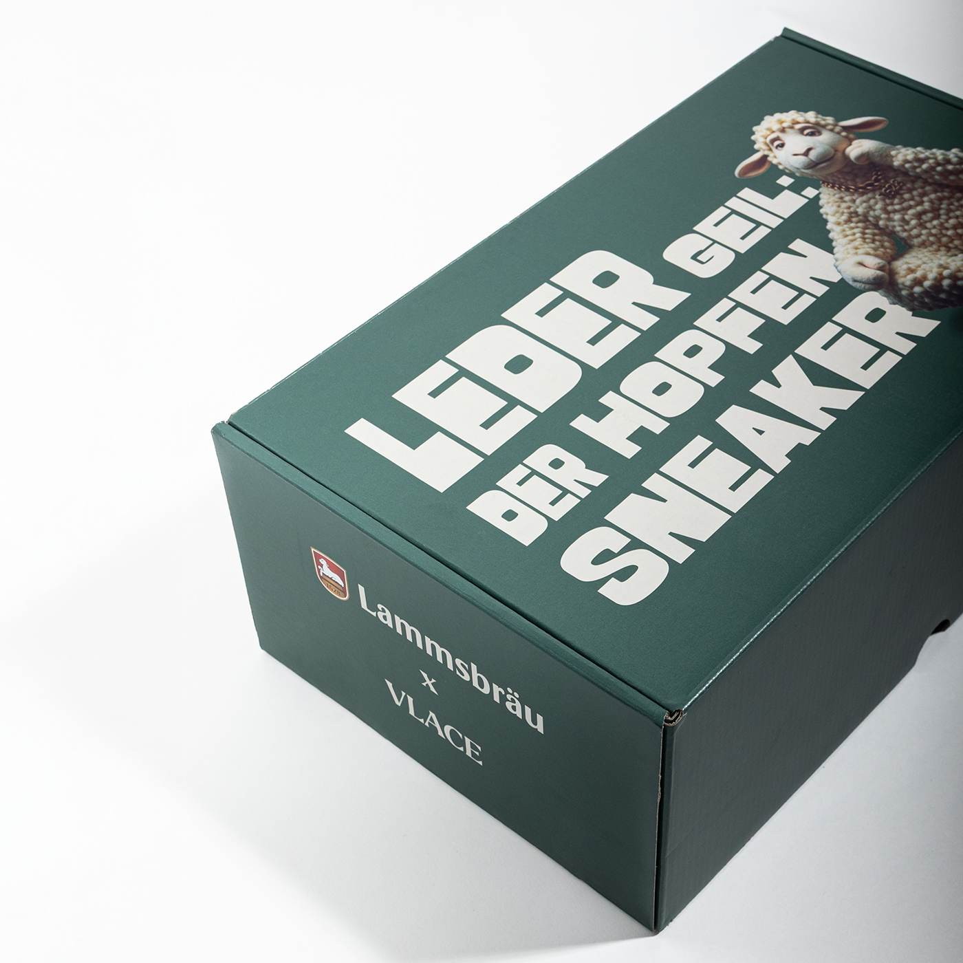 Auf dem Bild ist ein Schuhkarton zu sehen. Auf diesem Schuhkarton steht auf der oberen Fläche " LEDER GEIL: DER HOPFEN SNEAKER. Daneben ist "Lämmi", das Markentier der Brauerei, zu sehen.
Auf der Außenseite sieht man die Schriftzüge Lammsbräu x VLACE.