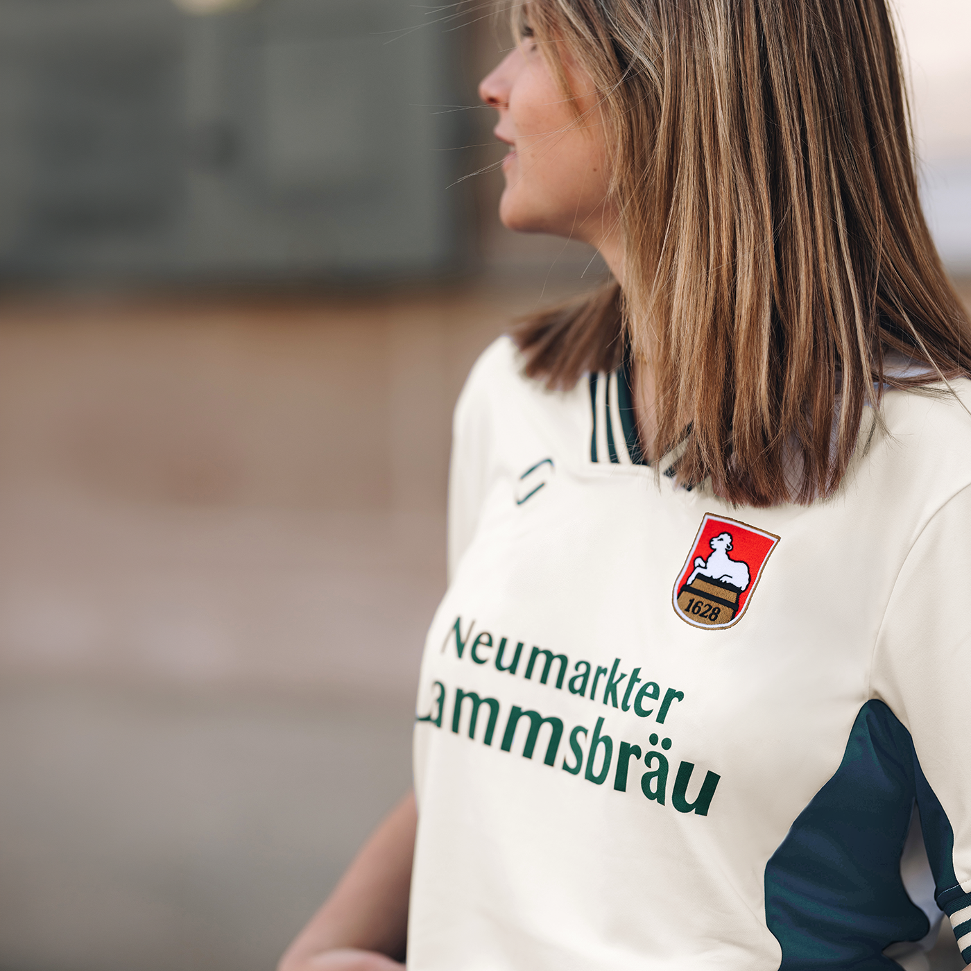 Ein weibliches Model trägt ein Retro-Fußballtrikot.  Das Bild ist abgeschnitten und man sieht das Model nicht ganz. Das Trikot ist im Farbton "elfenbein" und hat auf der Brust den Schriftzug "Neumarkter Lammsbräu". Außerdem sind das Logo von runamics und das Logo von Lammsbräu auf dem Trikot integriert.
